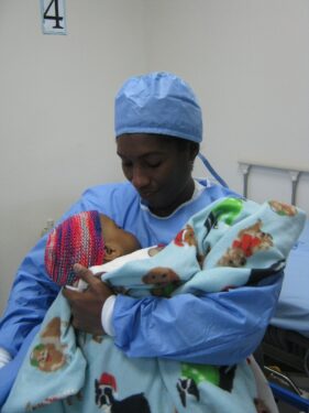 Mother wears surgical scrubs and holds her child after surgery.