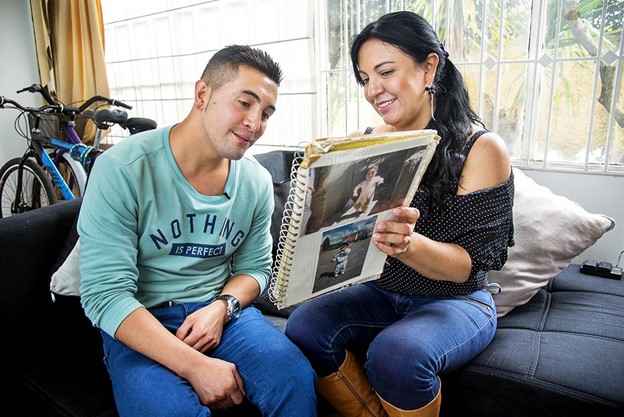A young man and his mother look at a photo album of old pictures.