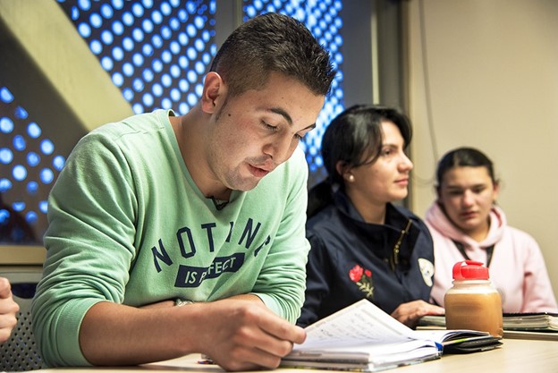 A young man in a green sweatshirt reads a textbook in a university classroom