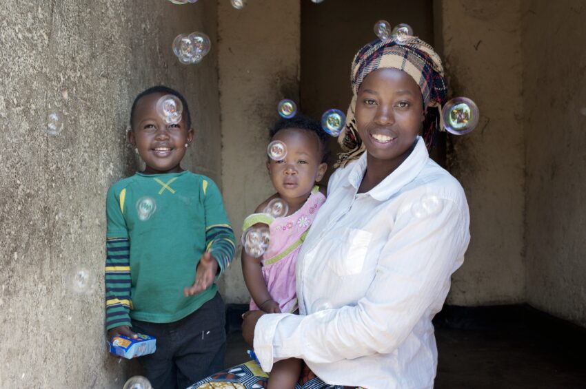 A Rwandan mother and her two children smile as bubbles float around them.