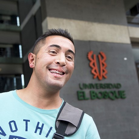 A young man smiles, showing his braces, in front of a university