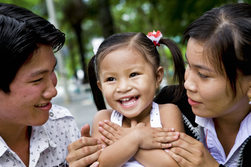 A 4-year-old Vietnamese cleft patient beams playfully, her joyful smile radiating as her parents look on with admiration.