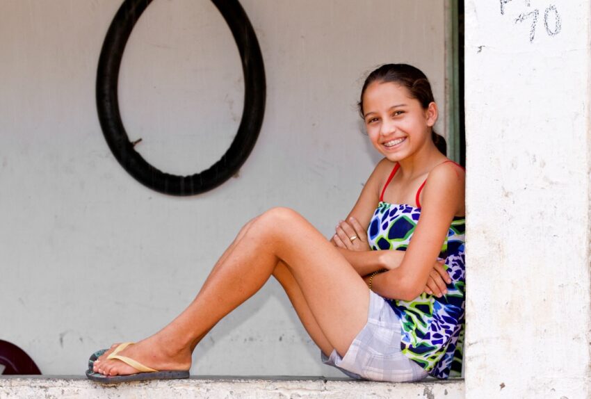 A young teenage girl smiles brightly while sitting on the edge of a wall.